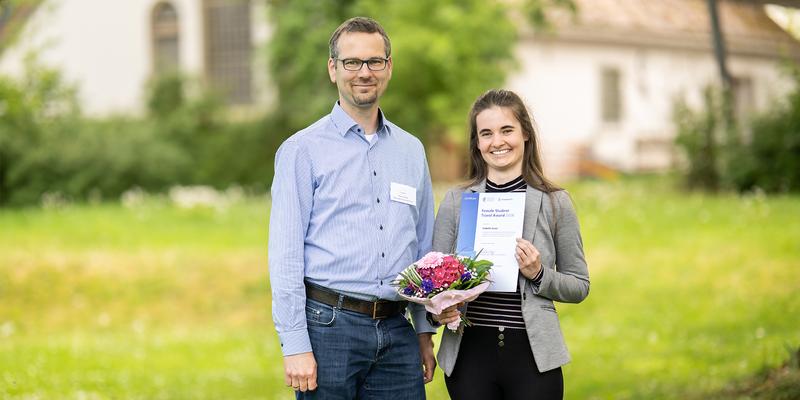 A woman and a man are standing side by side, holding the Female Student Travel Award