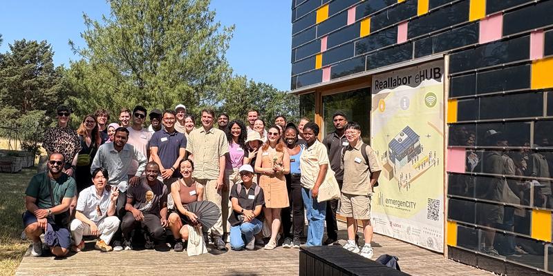 A group of 30 people in the sun in front of a building covered in solar panels
