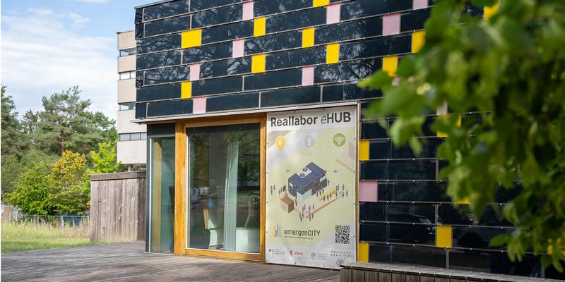 A small building whose exterior is completely covered with blue photovoltaic panels and small yellow and pink squares.