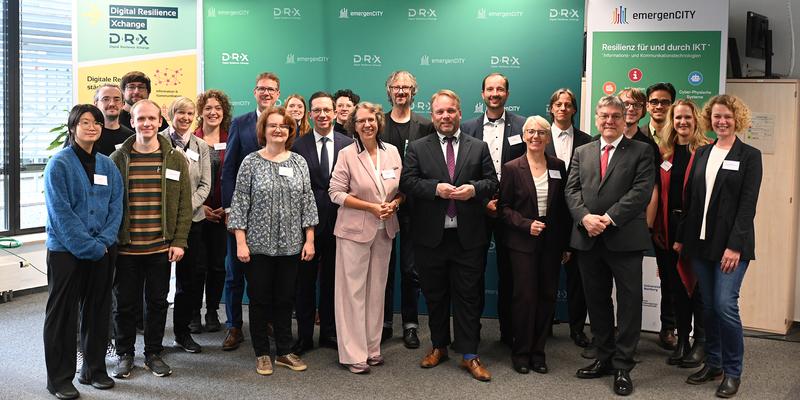 Gruppenfoto vor einer dreiteilingen grünen Wand mit emergenCITY und DiReX Logo mit rund 25 Personen.