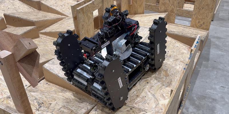 A robot with four belt wheels drives over an uneven plywood construction