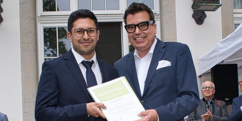 Zwei Männer halten eine Urkunde in der Hand.
