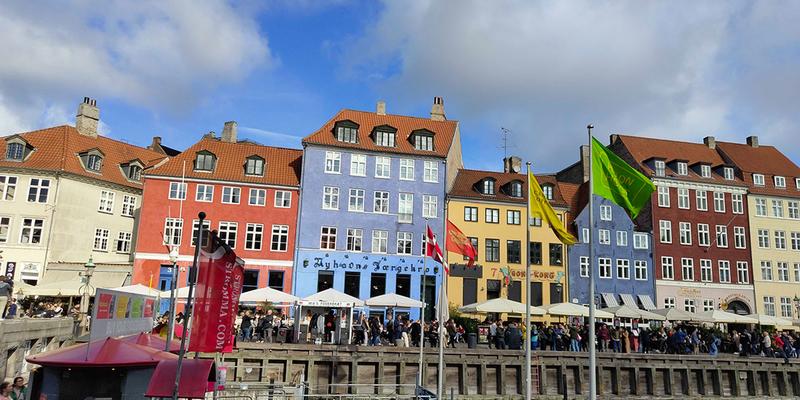 In Copenhagen, there is a row of colorful houses along a canal. In front of them, there is a lot of activity.