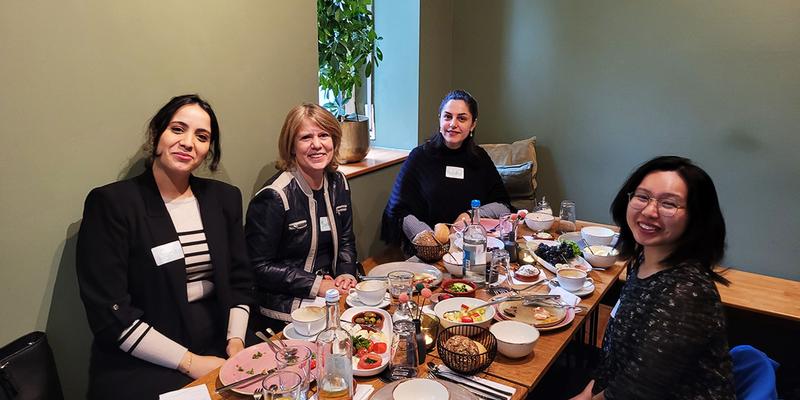 Vier Frauen sitzen an einem Tisch und lächeln in die Kamera.