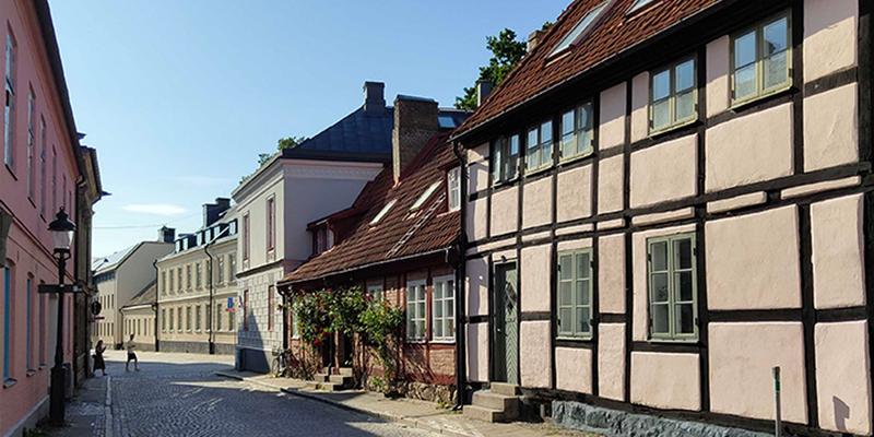 A quiet cobblestone street lined with historic half-timbered houses and pastel-colored buildings on a sunny day.