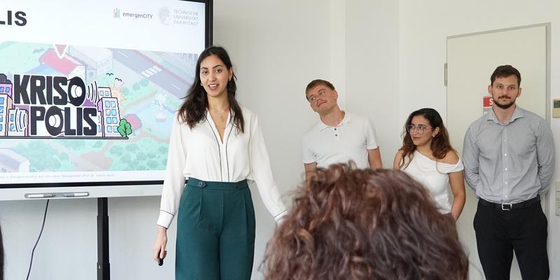 Four people in front of a smart board with a presentation, the back of a head in the foreground.