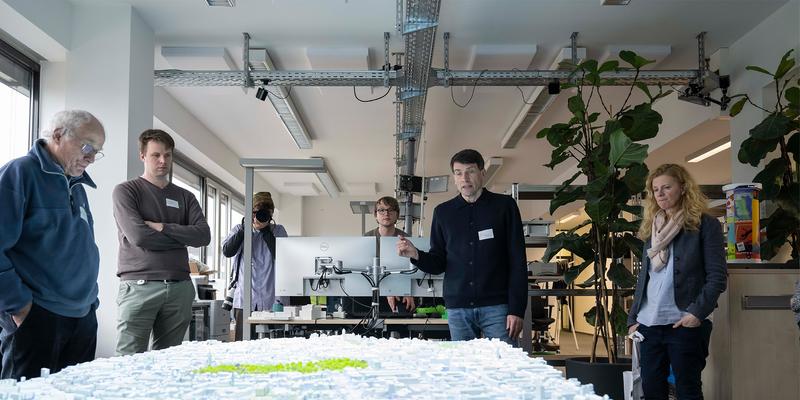 Four people are standing around a wooden model of a city onto which something is being projected.