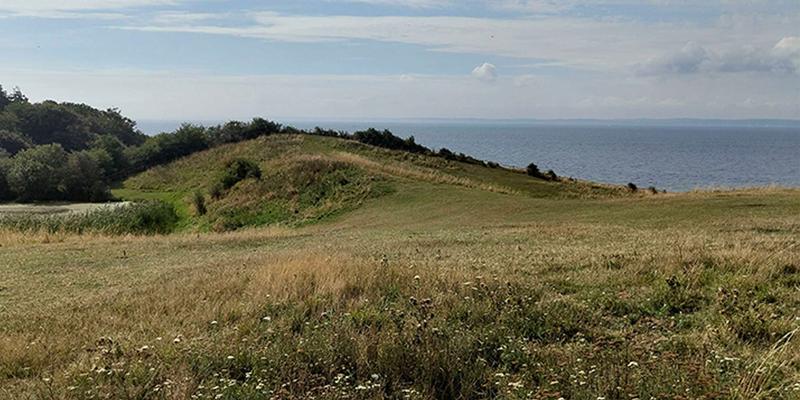 A hilly grassy landscape in front of the sea can be seen.