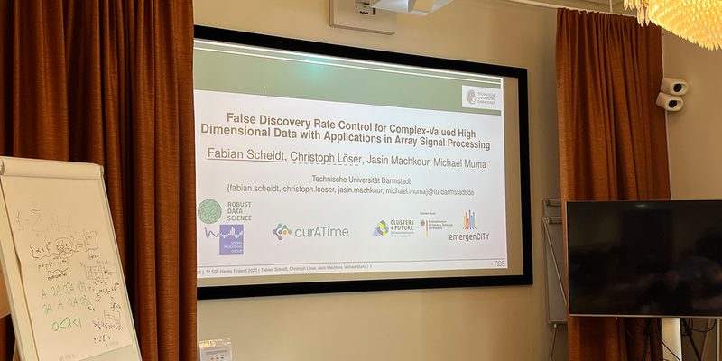 The cover picture of the presentation can be seen. Red curtains hang to the left and right of it, with a flipchart in the foreground.
